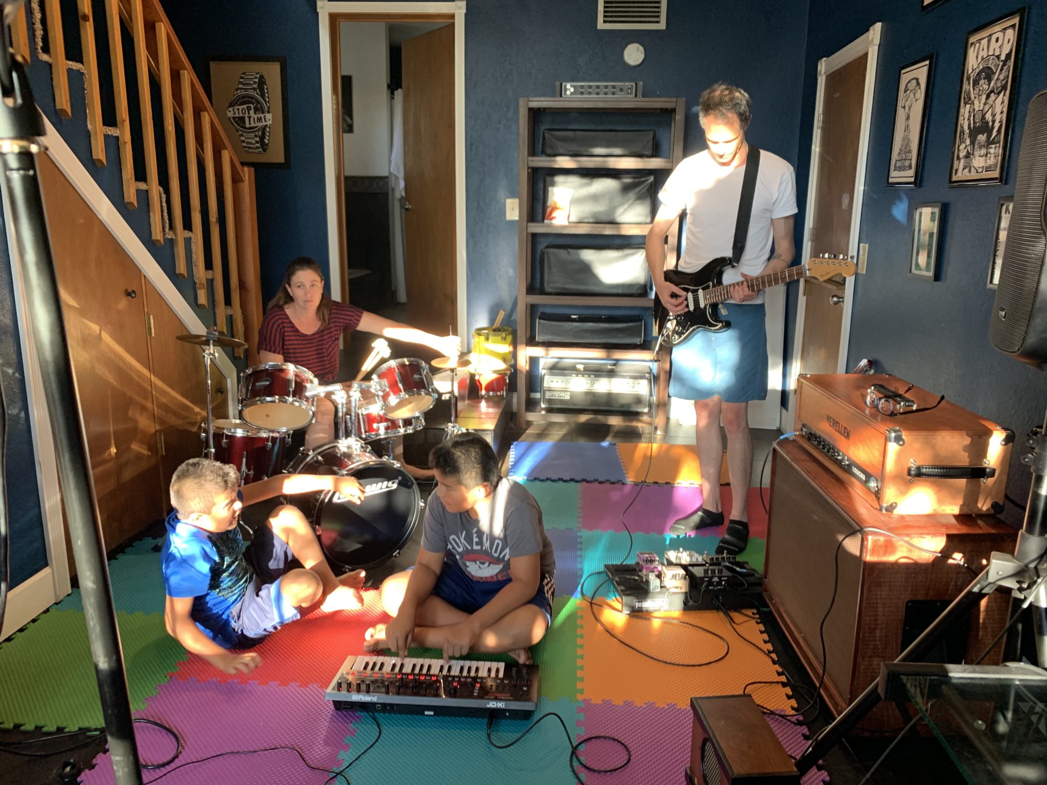Teacher on drums, a guitarist standing, and two kids on a foam floor, one playing keyboard