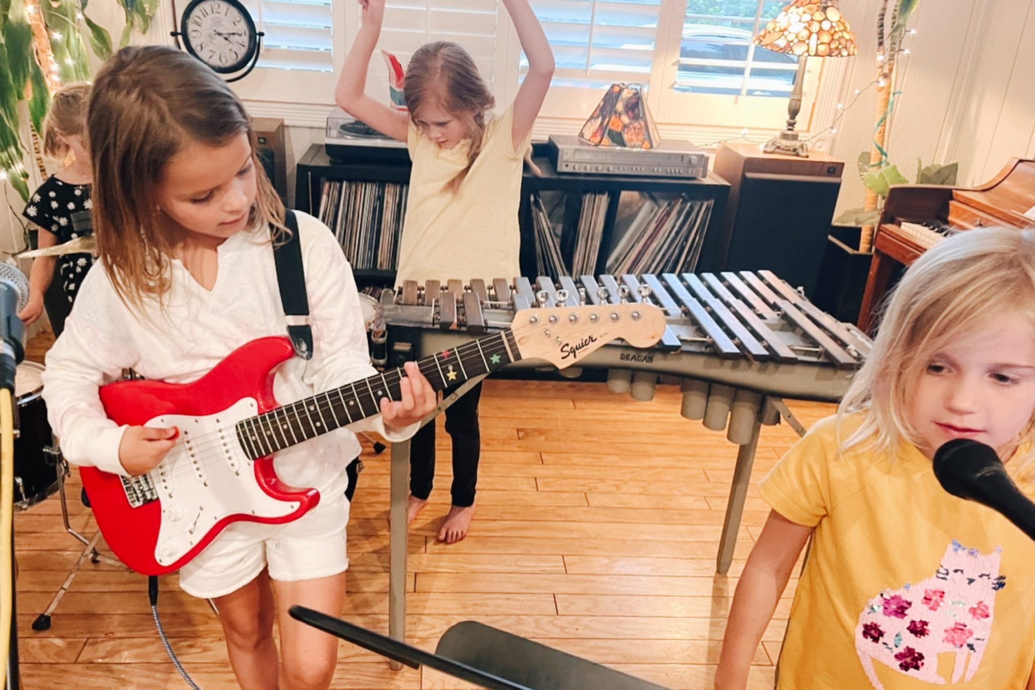 Kids playing a red electric guitar, singing at a microphone and dancing beside a vibraphone