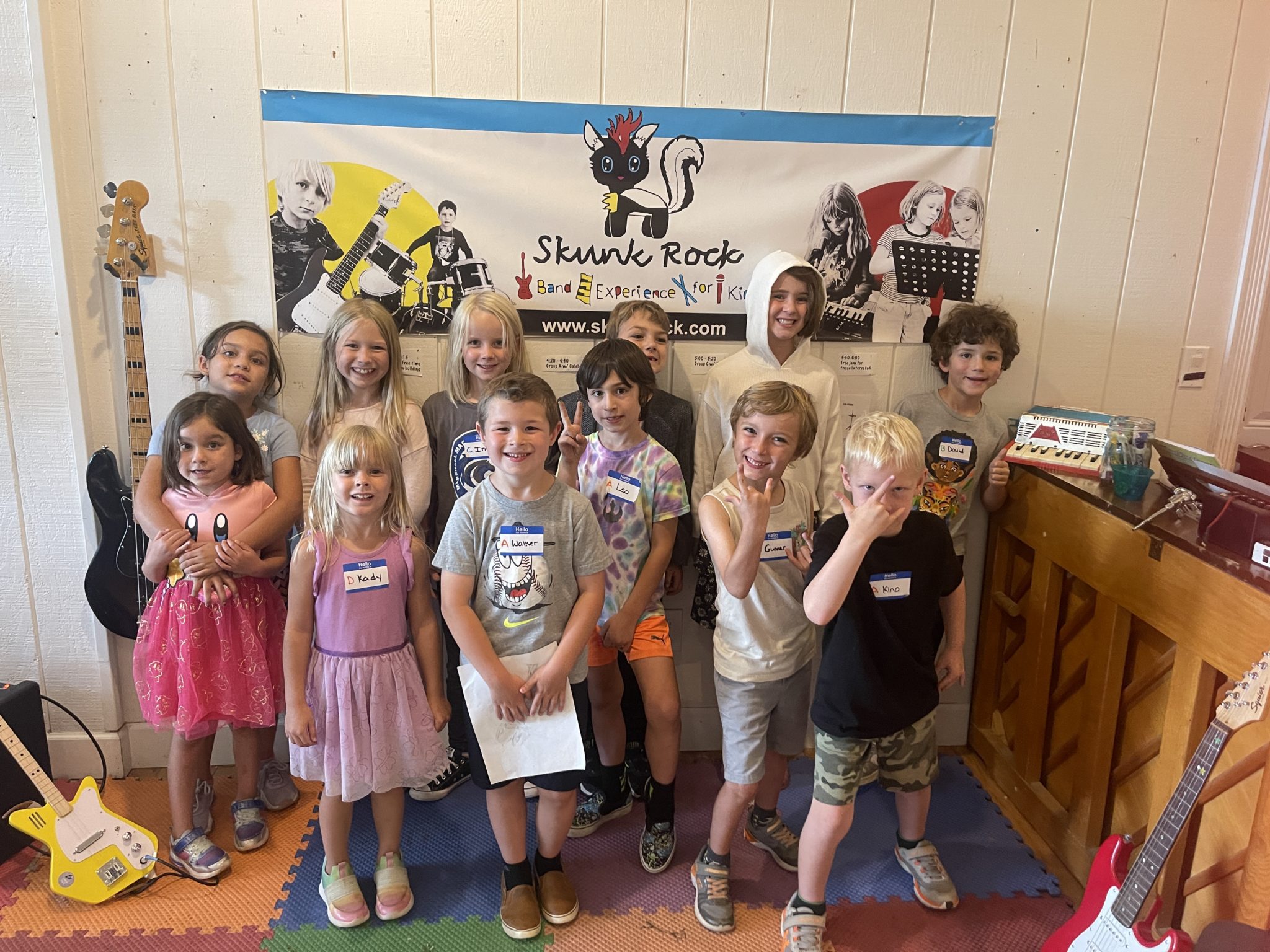 Group of smiling kids with name tags posing in front of a Skunk Rock banner