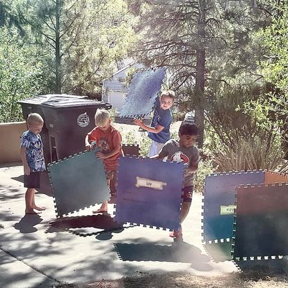 Four kids carrying large foam floor mats outdoors on a sunny day