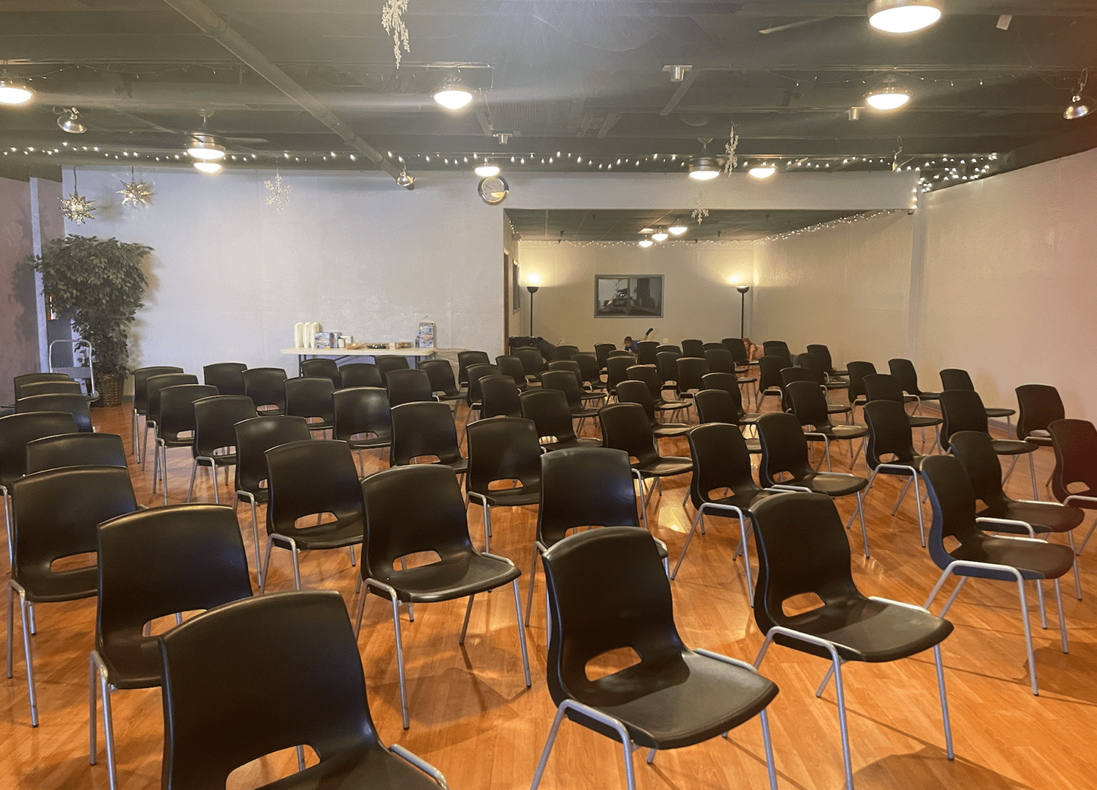Rows of empty black chairs in a hall with string lights and a snack table